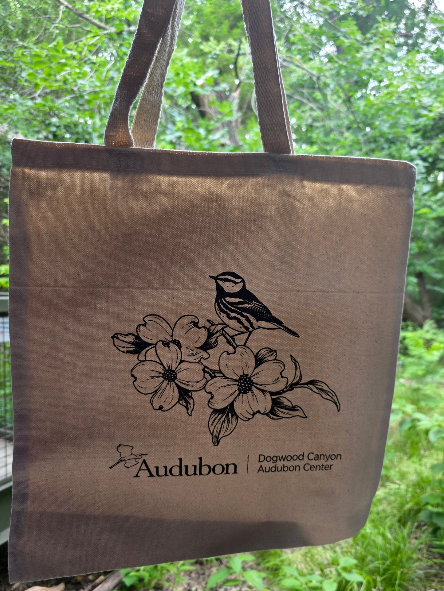 Canvas tote bag with bird and flower design and Audubon logo against a green outdoor background